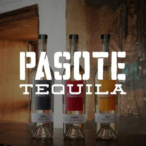 Drei Pasote-Tequila-Flaschen in klaren Glasflaschen mit unterschiedlich farbigen Etiketten nebeneinander auf einer Holzoberfläche vor einer rustikalen Bar-Kulisse präsentiert.